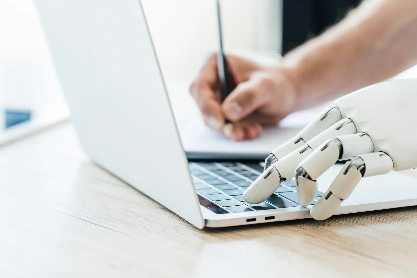 Human hand and robot hand typing on a laptop together